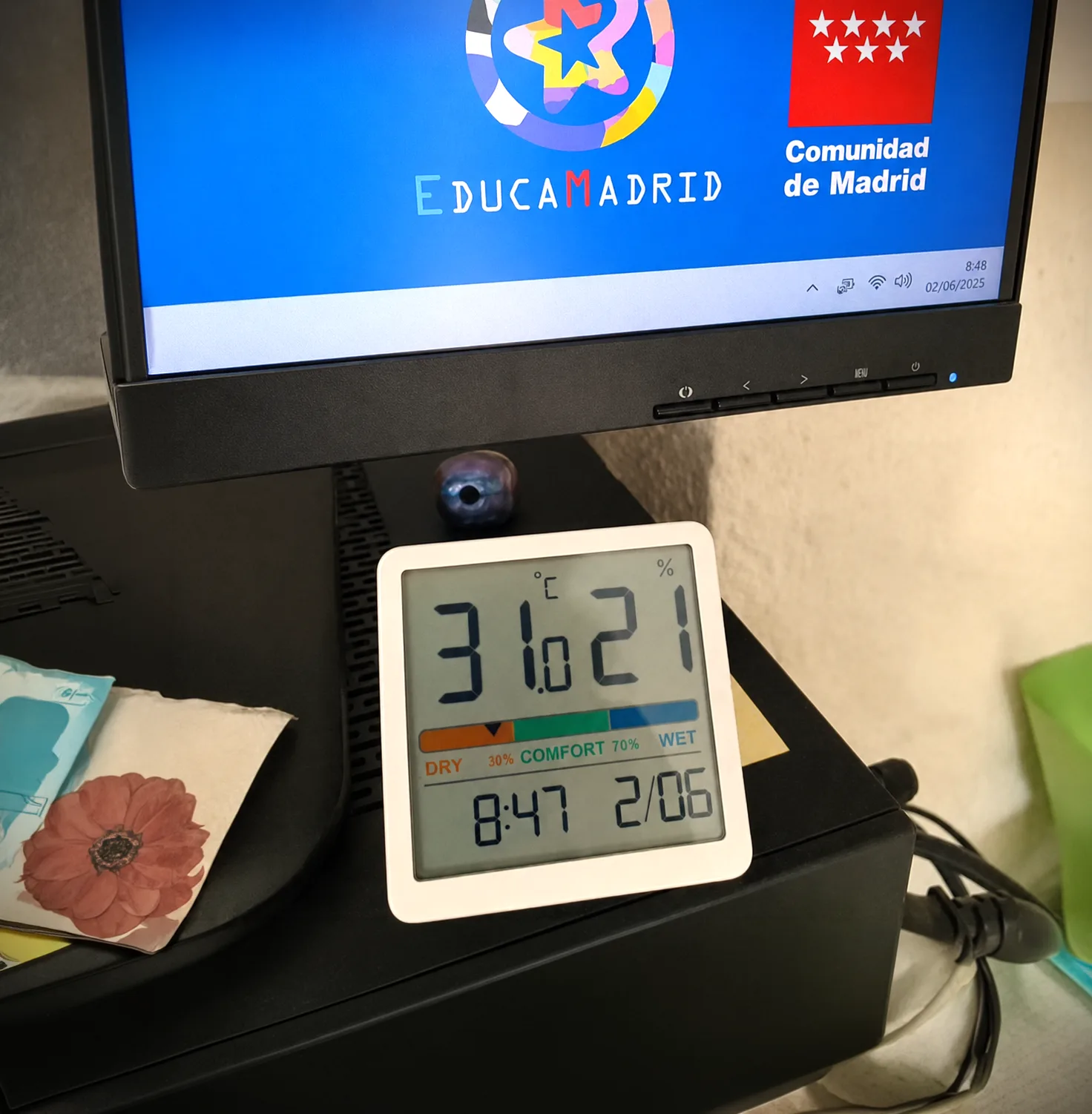 Termohigrometro marcando 31 grados junto a la pantalla de EducaMadrid
